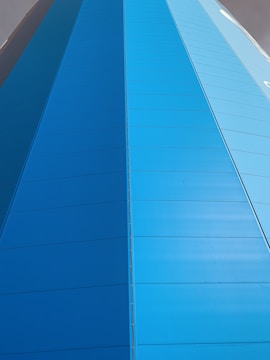 A tall structure featuring vertical panels in varying shades of blue, with a sleek and modern appearance. The structure tapers toward the top, creating a sense of height and depth.