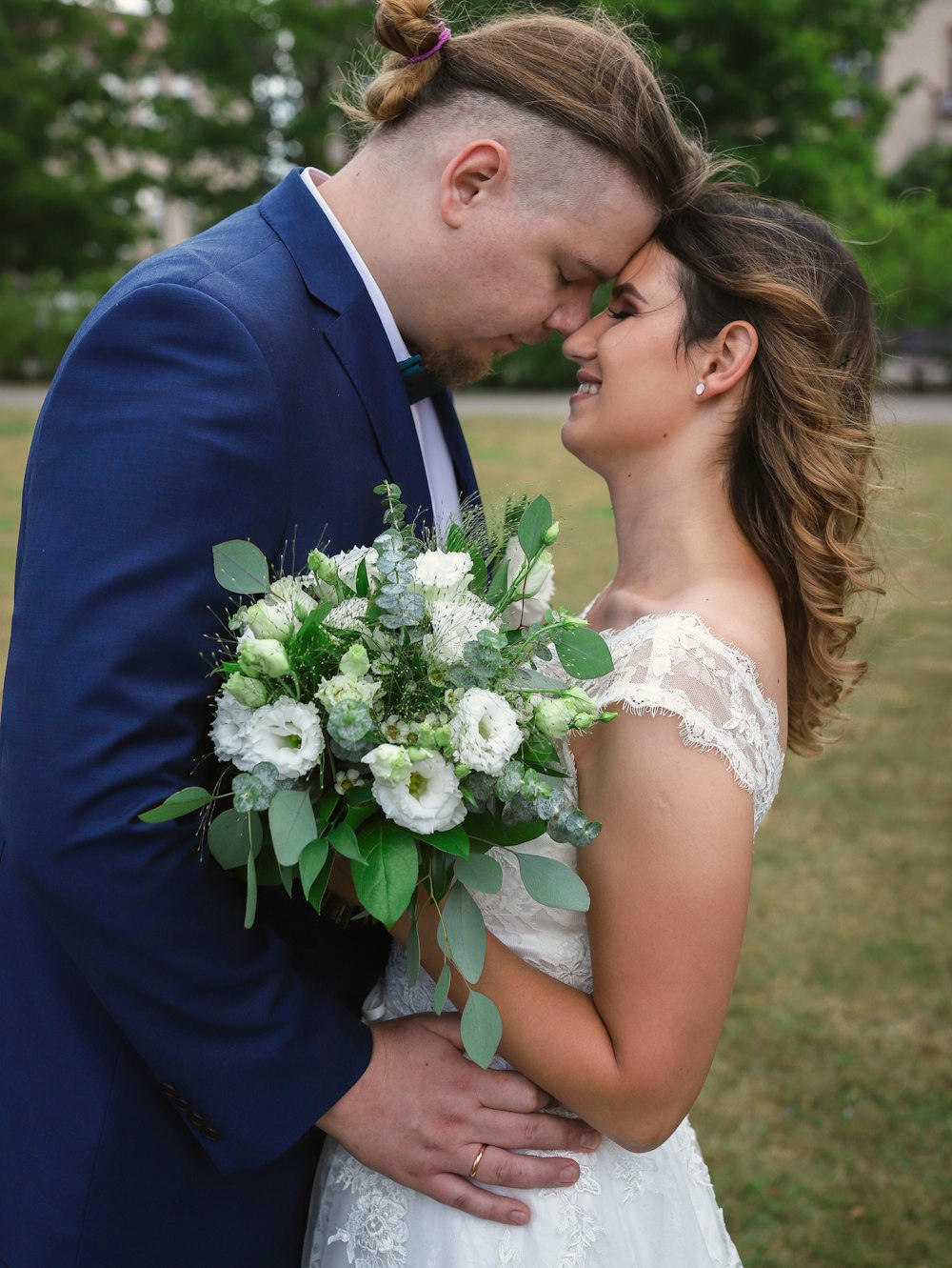 man in blue suit kissing woman in white floral wedding dress