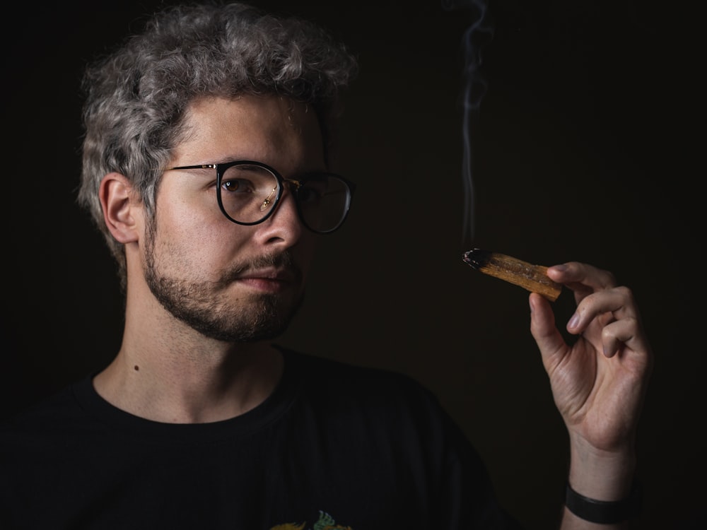 man in black crew neck shirt holding brown cigarette stick