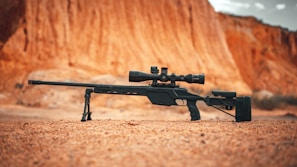 Operator adjusting a high-tech scope on a long-range precision rifle against a backdrop of a desert training range.