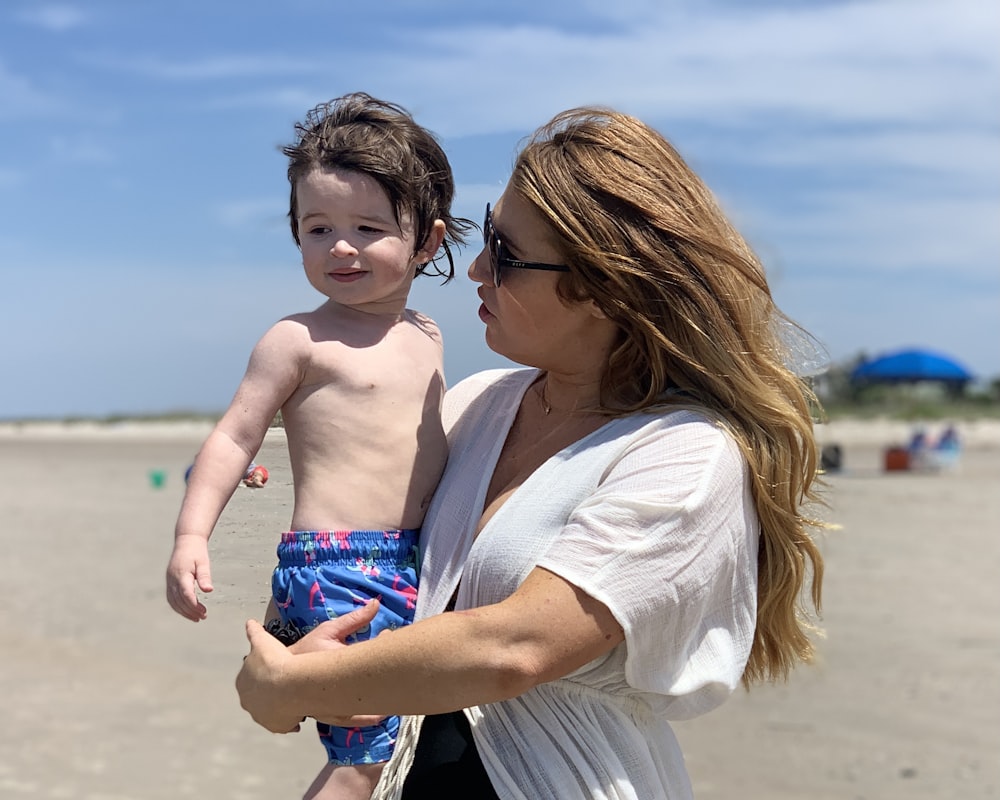 woman in white shirt carrying boy in blue and white shorts