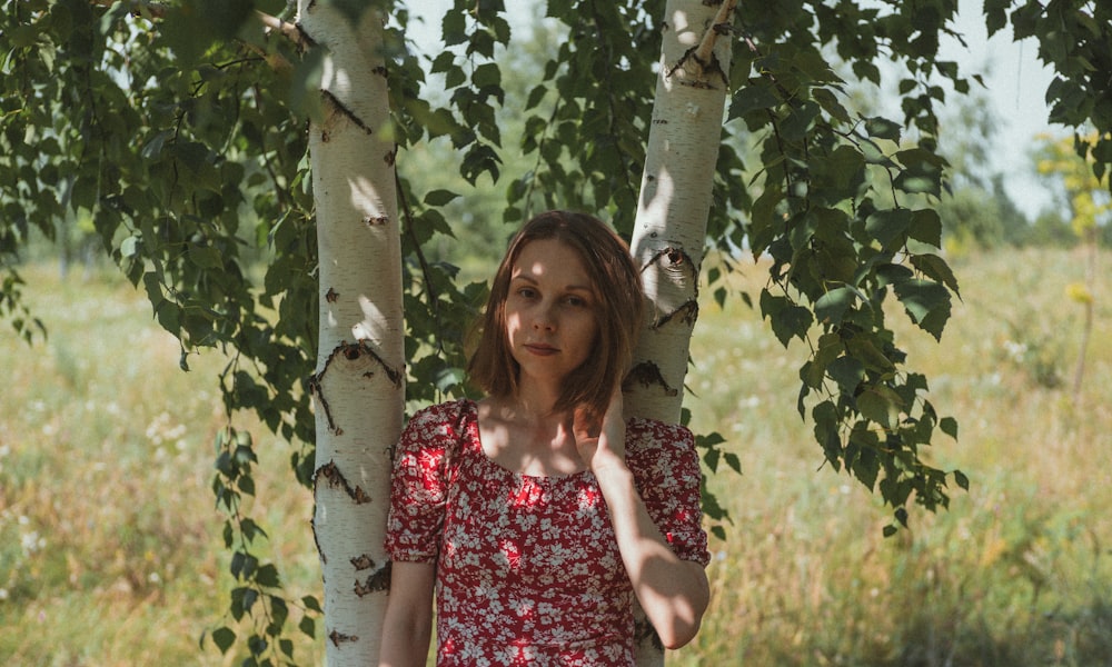woman in red and white floral dress standing beside green tree during daytime
