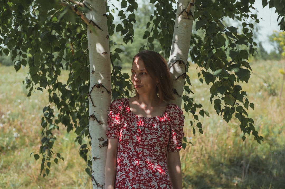 woman in red and white floral dress standing beside tree during daytime