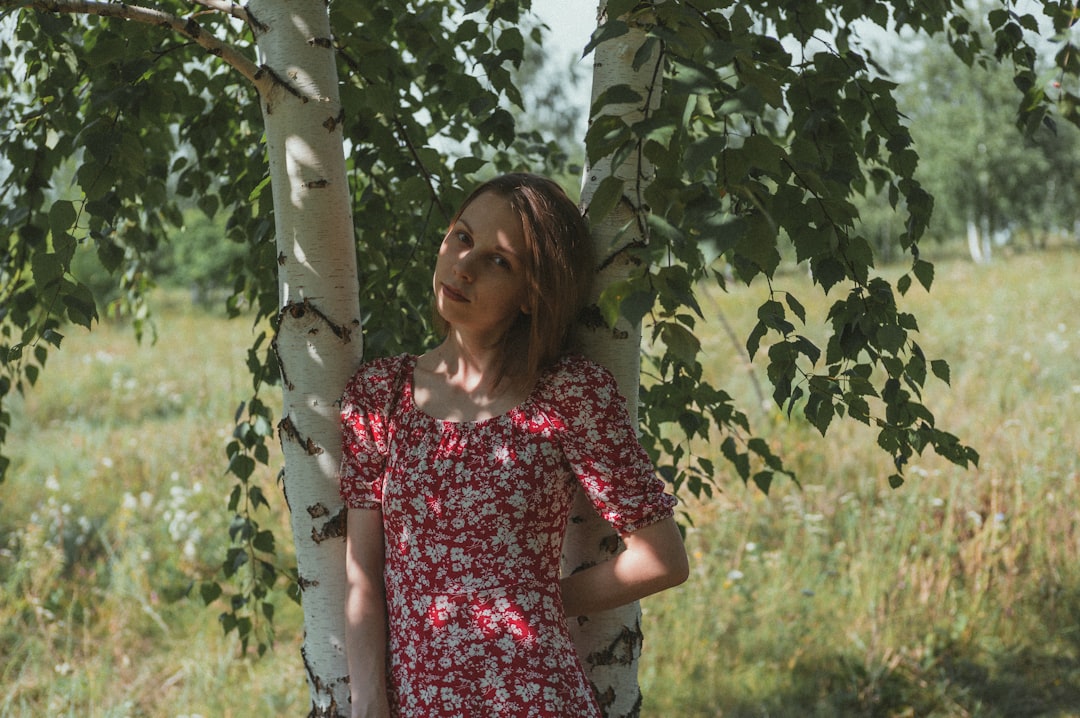 woman in red and white floral dress standing beside green leaf tree during daytime