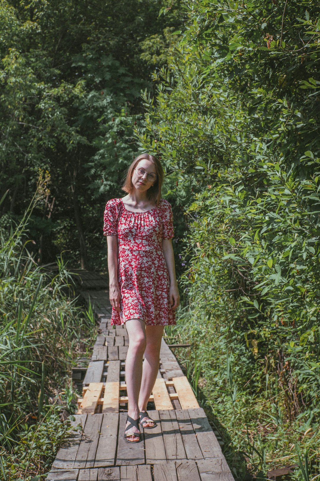 woman in purple and white floral dress standing on wooden pathway surrounded by green plants during