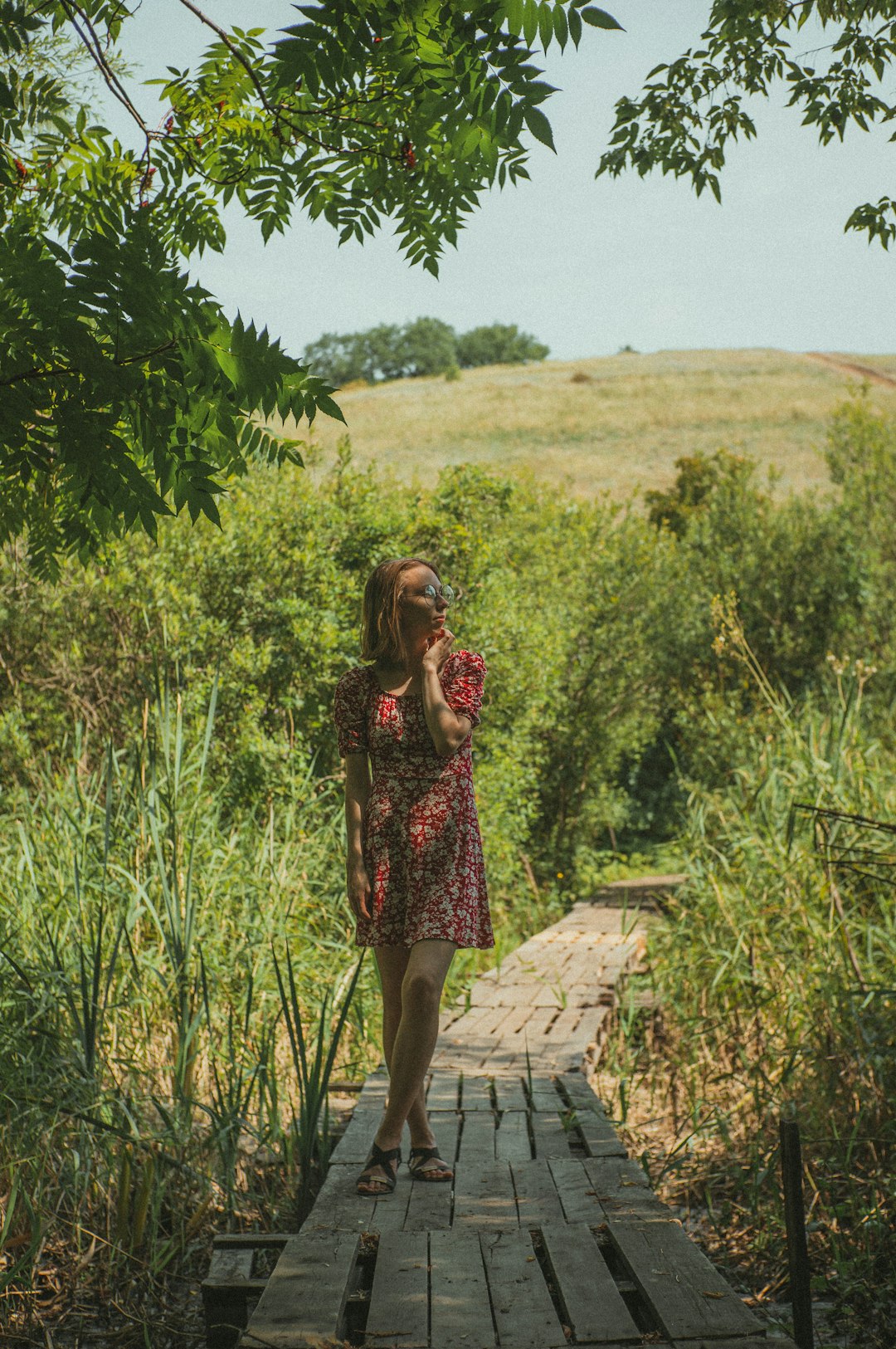 woman in red and black floral dress standing on concrete pathway between green grass field during