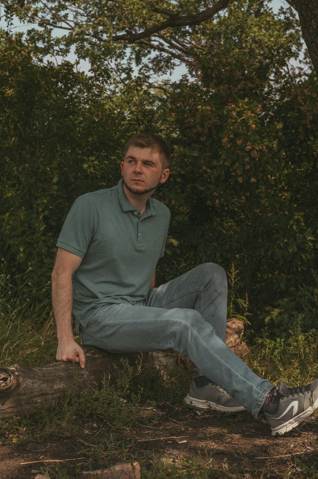 man in green polo shirt and blue denim jeans sitting on brown rock