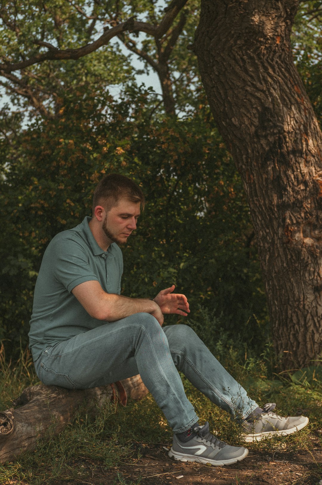 man in green crew neck t-shirt and blue denim jeans sitting on brown tree branch