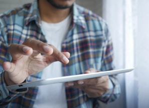 man in red and blue plaid button up shirt holding white tablet computer