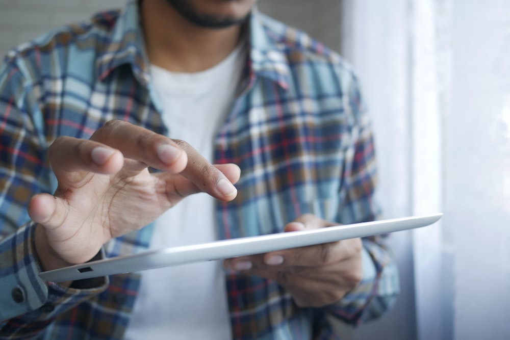 homem em vermelho e azul xadrez botão até camisa segurando computador tablet branco