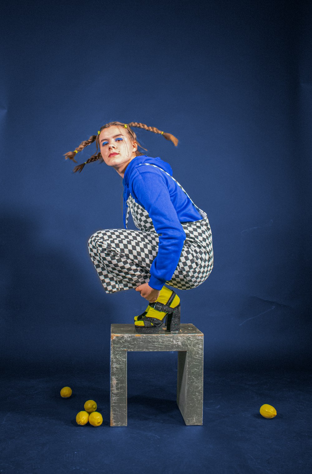 Femme en veste bleue et pantalon noir et blanc assise sur une boîte noire et jaune