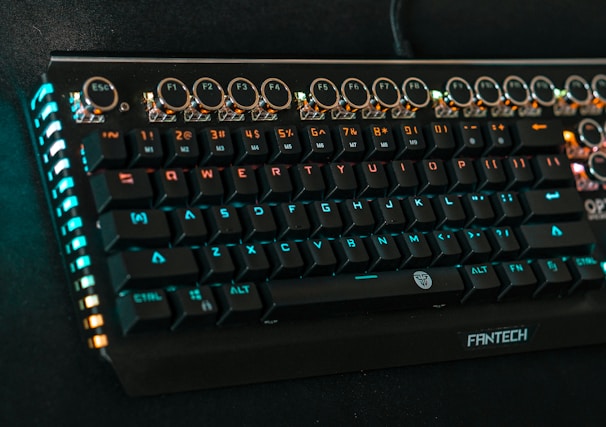 A mechanical keyboard with rounded, raised keys and a retro design, featuring multicolored backlighting, predominantly blue and orange. Function keys and a numeric row are visible at the top, with the brand name 'FANTECH' displayed on the front.