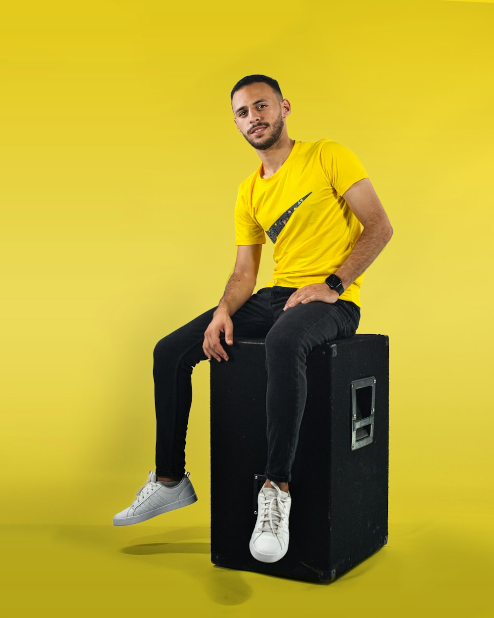 man in yellow crew neck t-shirt and black pants sitting on black box