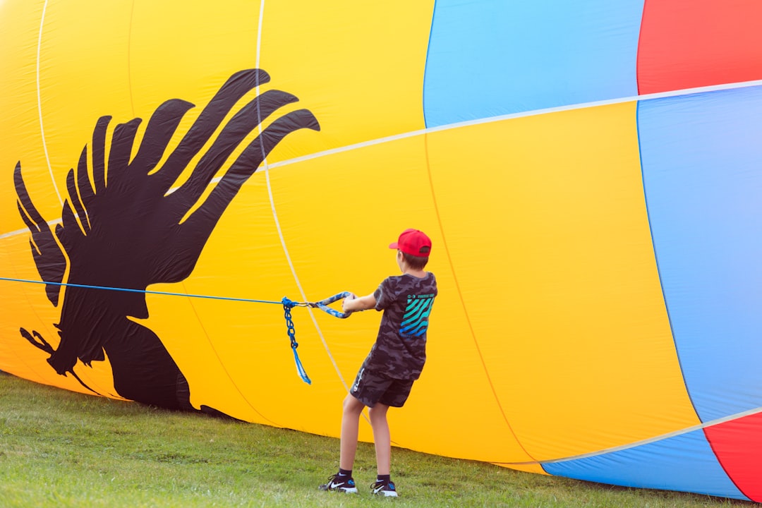 boy in green shirt and brown shorts holding yellow and blue hot air balloon