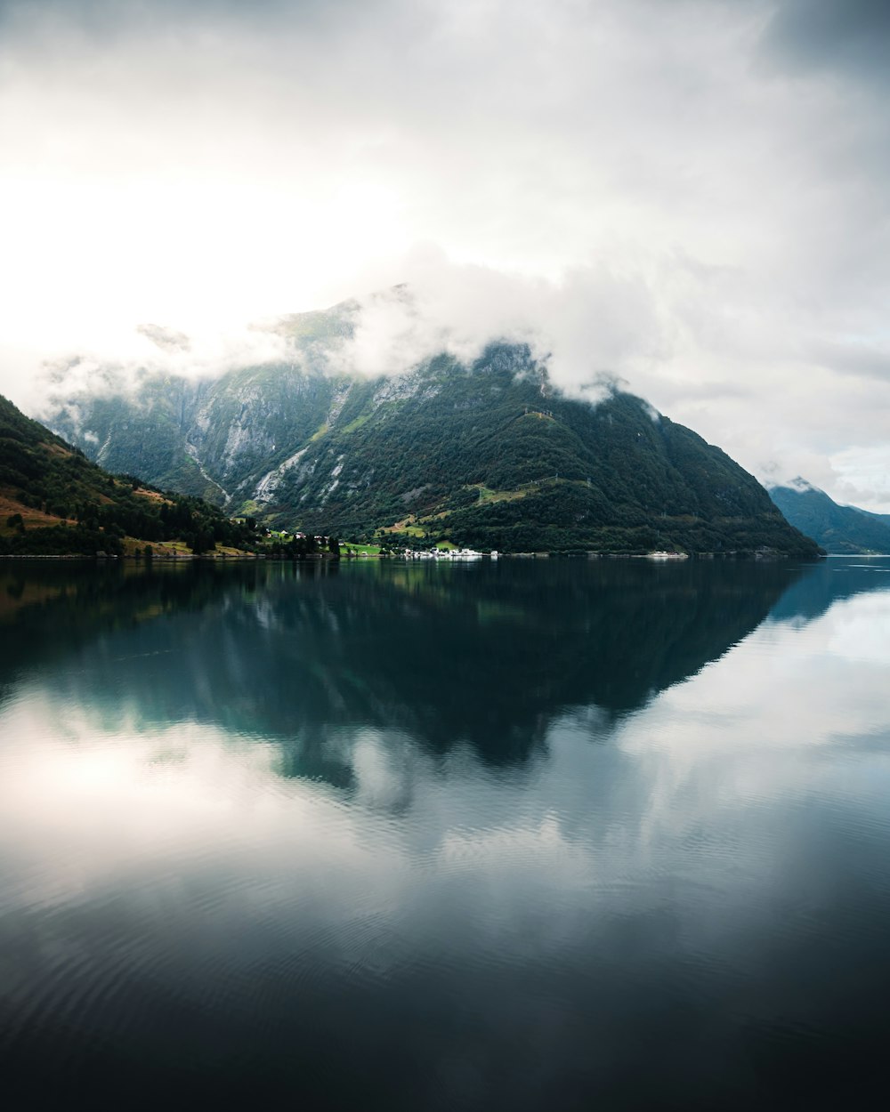 green and brown mountain beside lake under white clouds during daytime