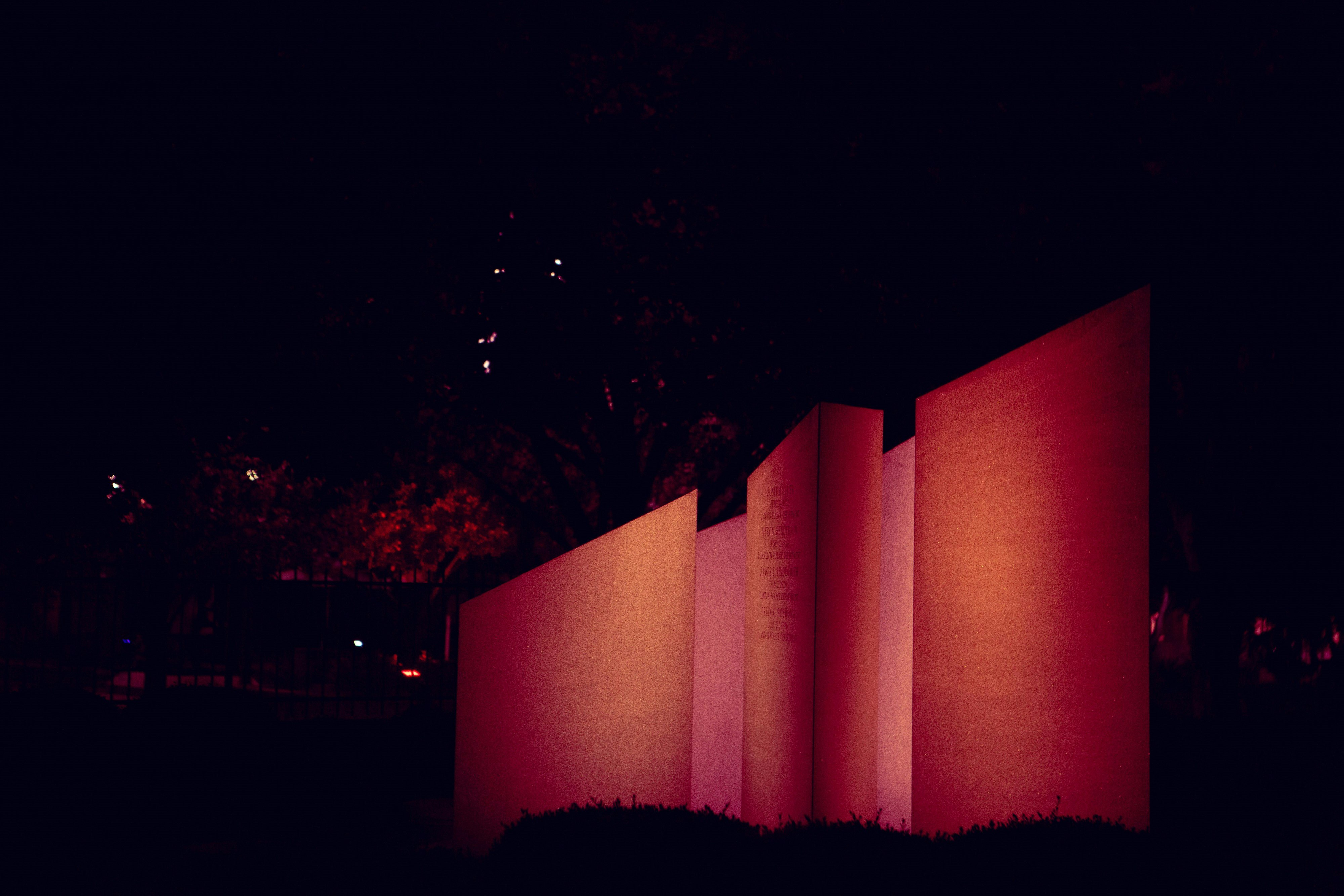 A lit, reddish, monument sits quietly on a warm, lonely, summer's night. 