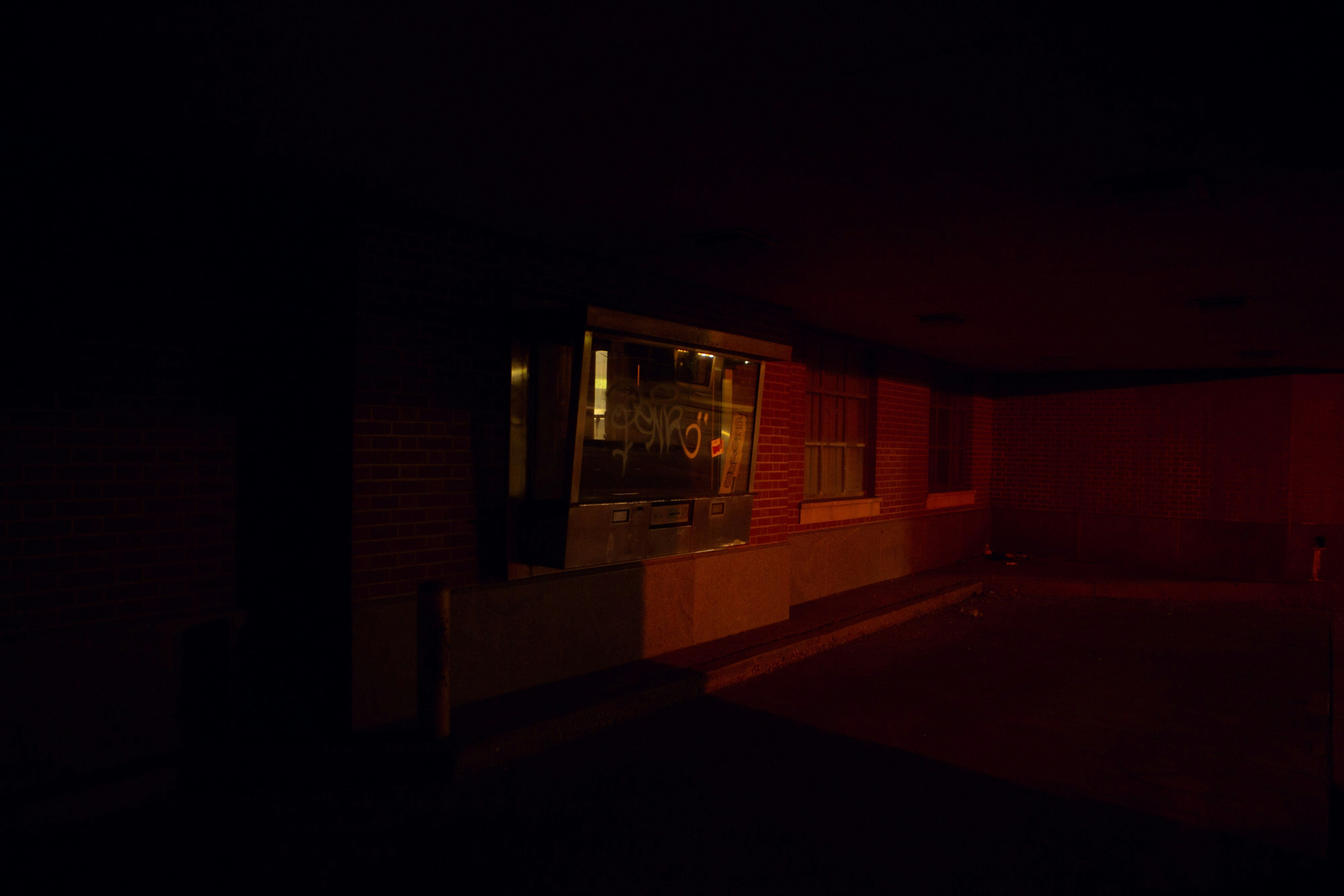 An old bank teller drive through sits empty in a dark, red, alley. 
