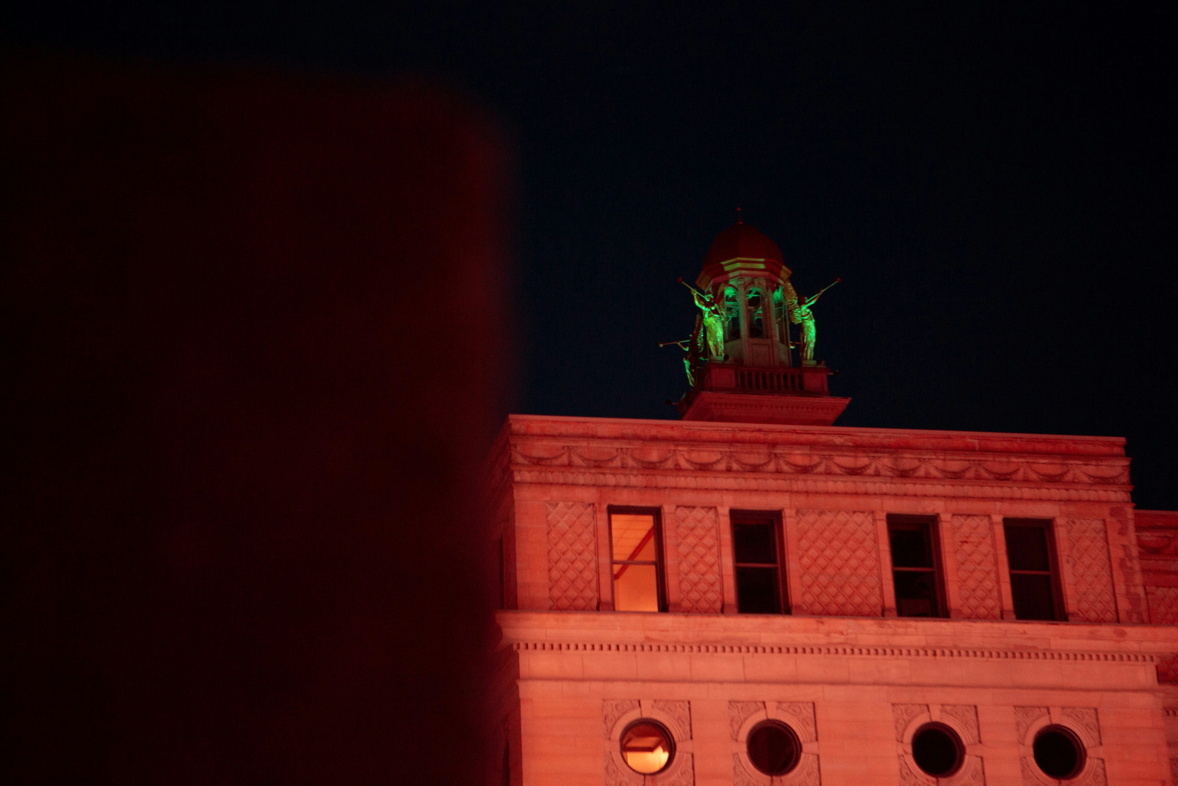 Light with green lights, a group of angels silently blow their horns on top of a city building. 