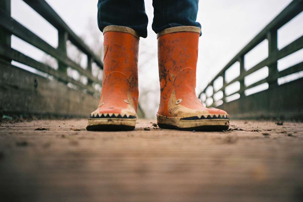 person in brown leather boots standing on brown wooden bridge