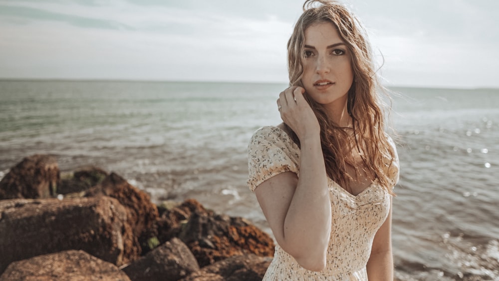 woman in white lace dress sitting on rock near sea during daytime