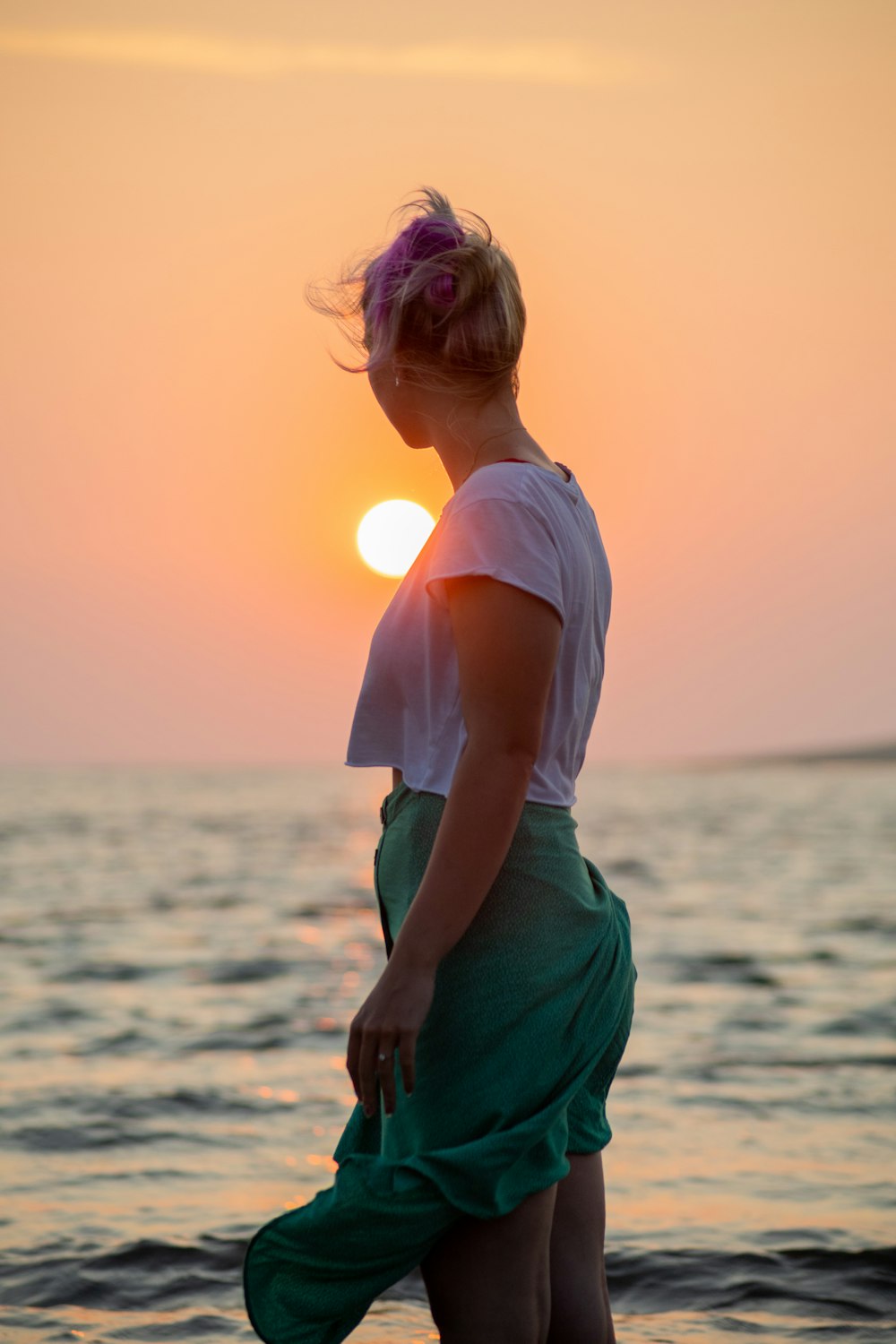 Femme en chemise blanche et jupe verte debout sur la plage au coucher du soleil