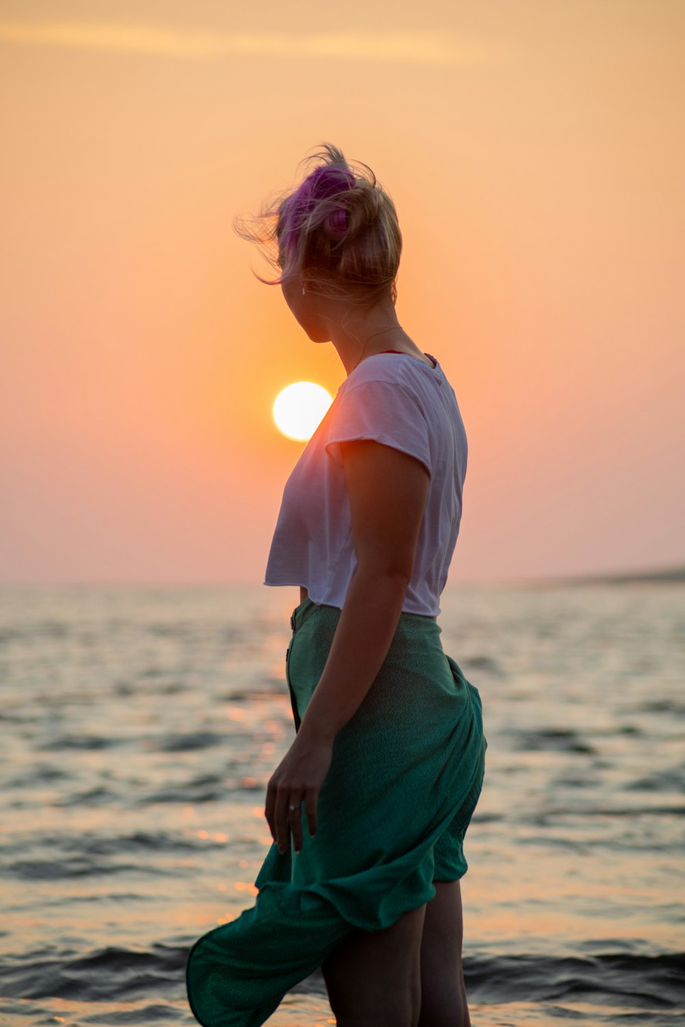 woman in white shirt and green skirt standing on beach during sunset