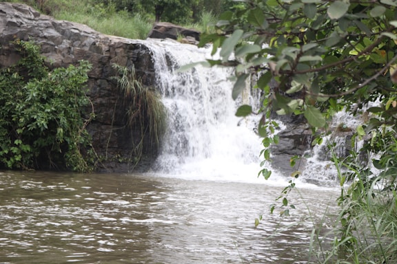 A serene view of a waterfall surrounded by lush greenery and rocks.