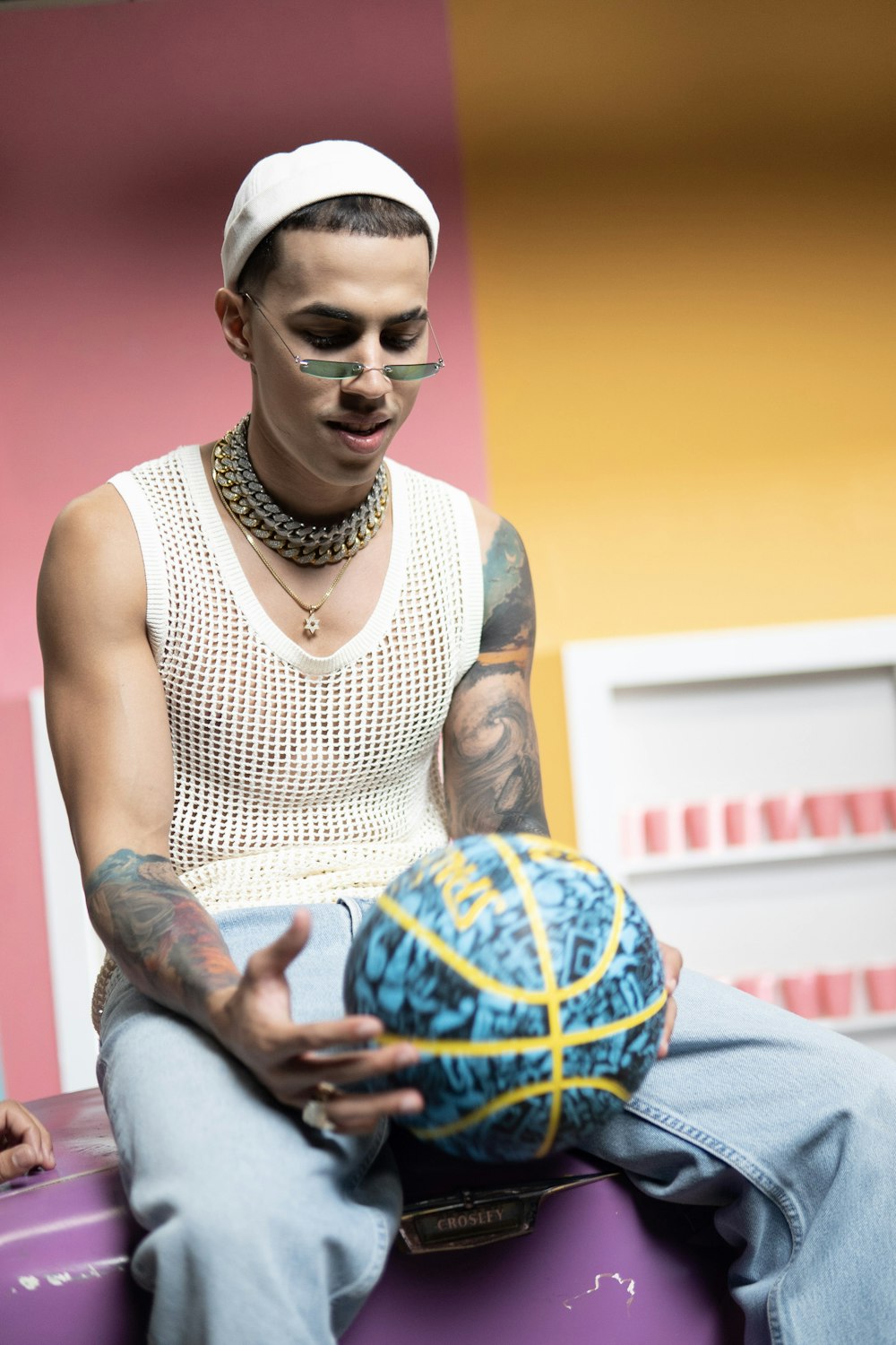 homme en débardeur blanc tenant un ballon de basket-ball bleu et orange