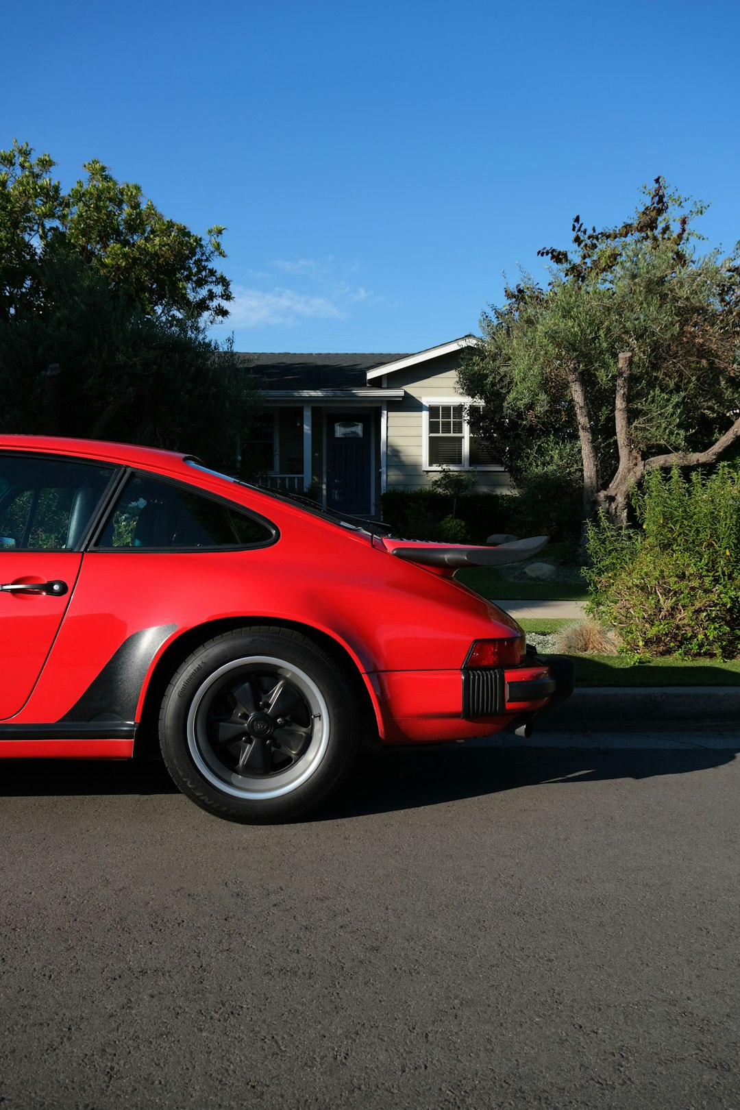 red sedan parked near green tree during daytime