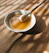 Close-up of a smiling man enjoying a spoonful of golden honey in a warm kitchen setting.