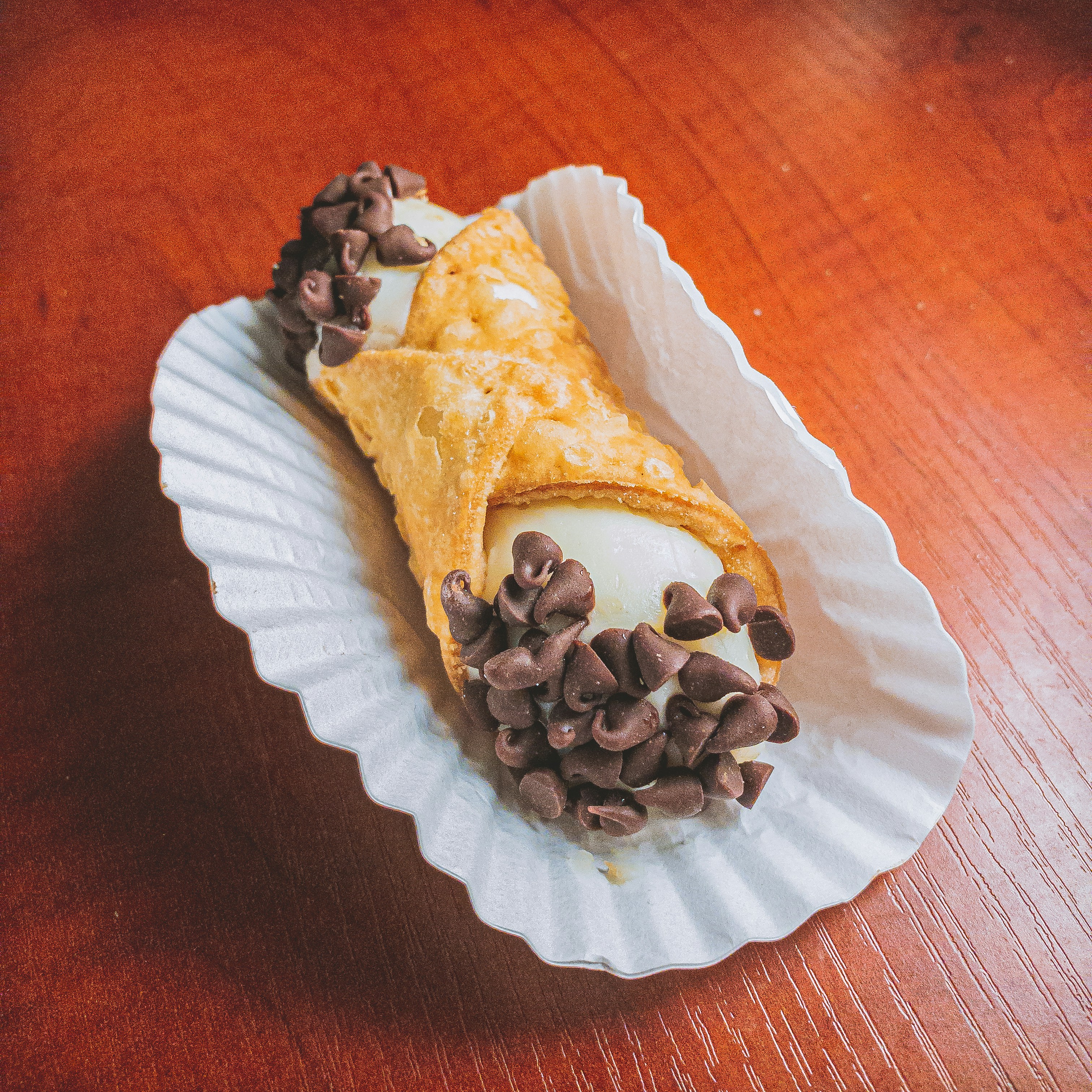 Two Sicilian cannoli filled with sweet ricotta and chocolate chips on a wooden board