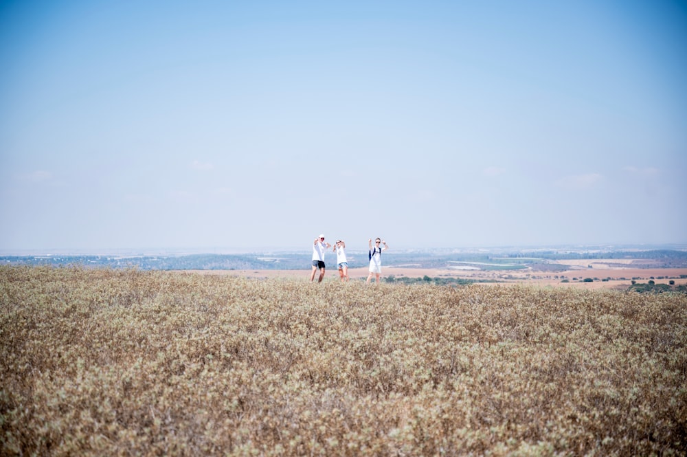 2 women and man walking on brown field during daytime