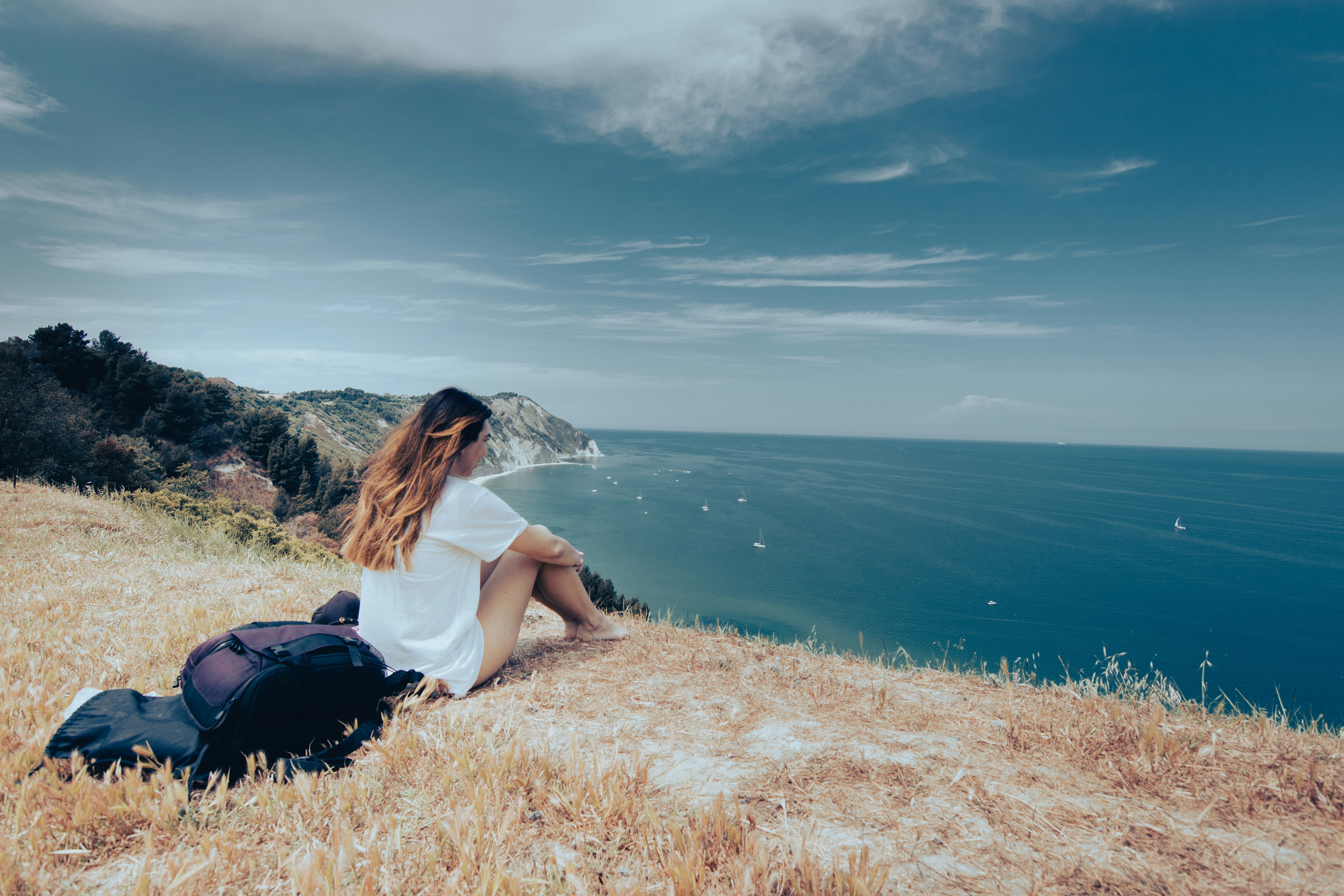 woman in white shirt sitting on brown grass field near body of water during daytime