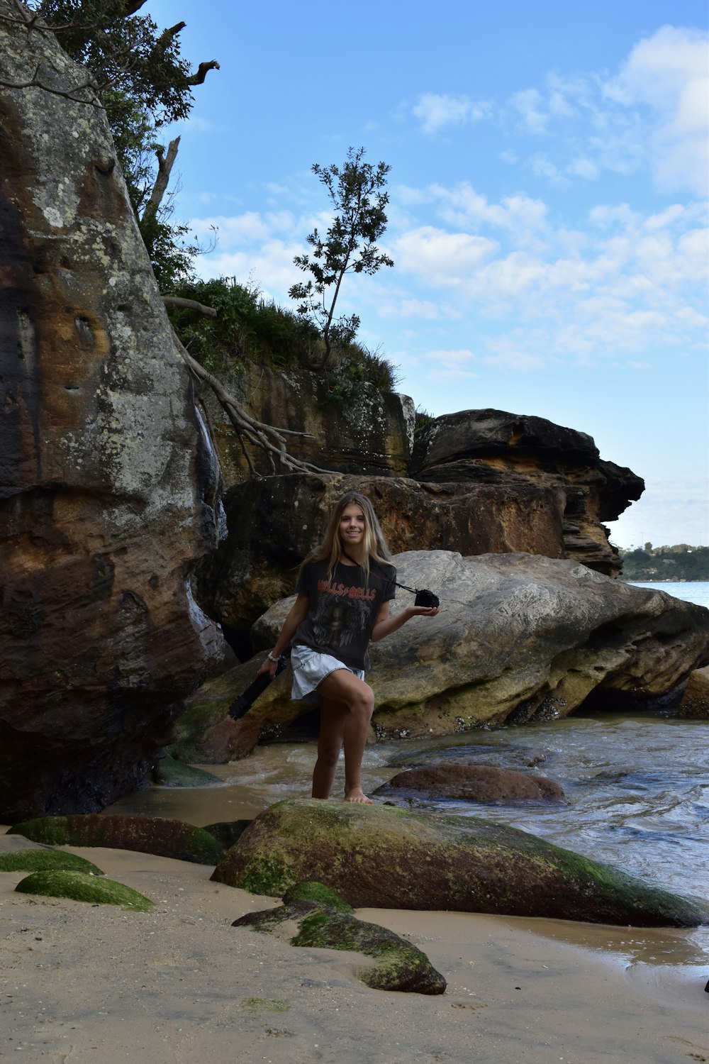 woman in black tank top and black shorts sitting on rock formation near body of water