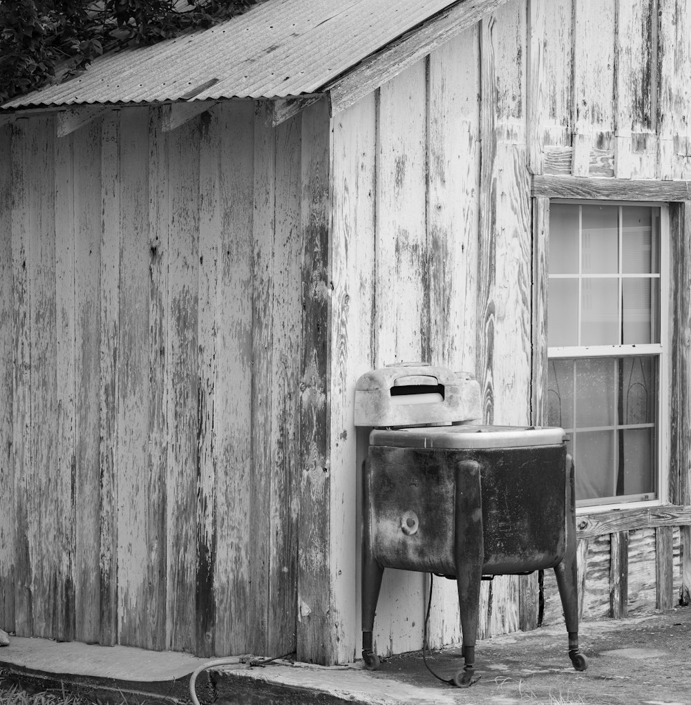 grayscale photo of black plastic trash bin beside wooden fence