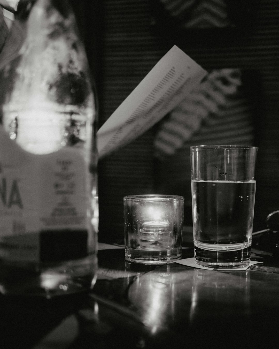 grayscale photo of clear drinking glass beside glass bottle