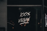 A neon sign displaying the phrase '100% Vegan' is illuminated against a dark background, likely in a storefront window.