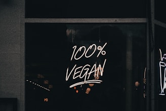 A neon sign displaying the phrase '100% Vegan' is illuminated against a dark background, likely in a storefront window.