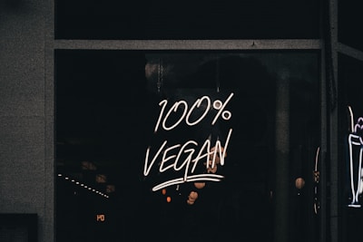 A neon sign displaying the phrase '100% Vegan' is illuminated against a dark background, likely in a storefront window.