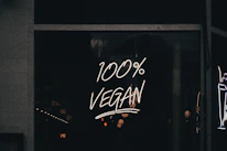 A neon sign displaying the phrase '100% Vegan' is illuminated against a dark background, likely in a storefront window.