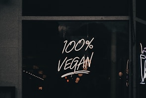 A neon sign displaying the phrase '100% Vegan' is illuminated against a dark background, likely in a storefront window.