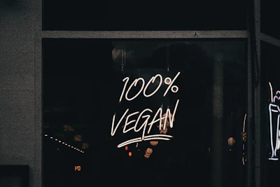 A neon sign displaying the phrase '100% Vegan' is illuminated against a dark background, likely in a storefront window.