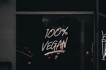 A neon sign displaying the phrase '100% Vegan' is illuminated against a dark background, likely in a storefront window.