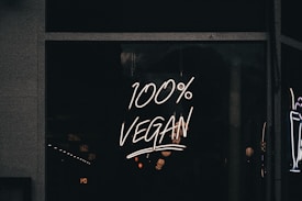 A neon sign displaying the phrase '100% Vegan' is illuminated against a dark background, likely in a storefront window.