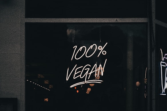 A neon sign displaying the phrase '100% Vegan' is illuminated against a dark background, likely in a storefront window.
