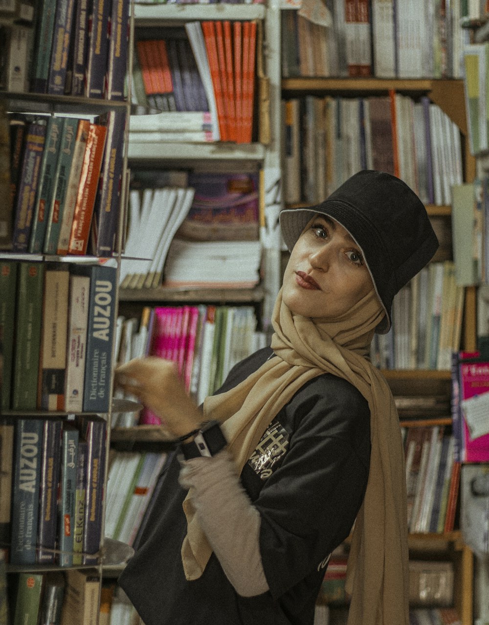woman in black knit cap and black jacket standing in front of books