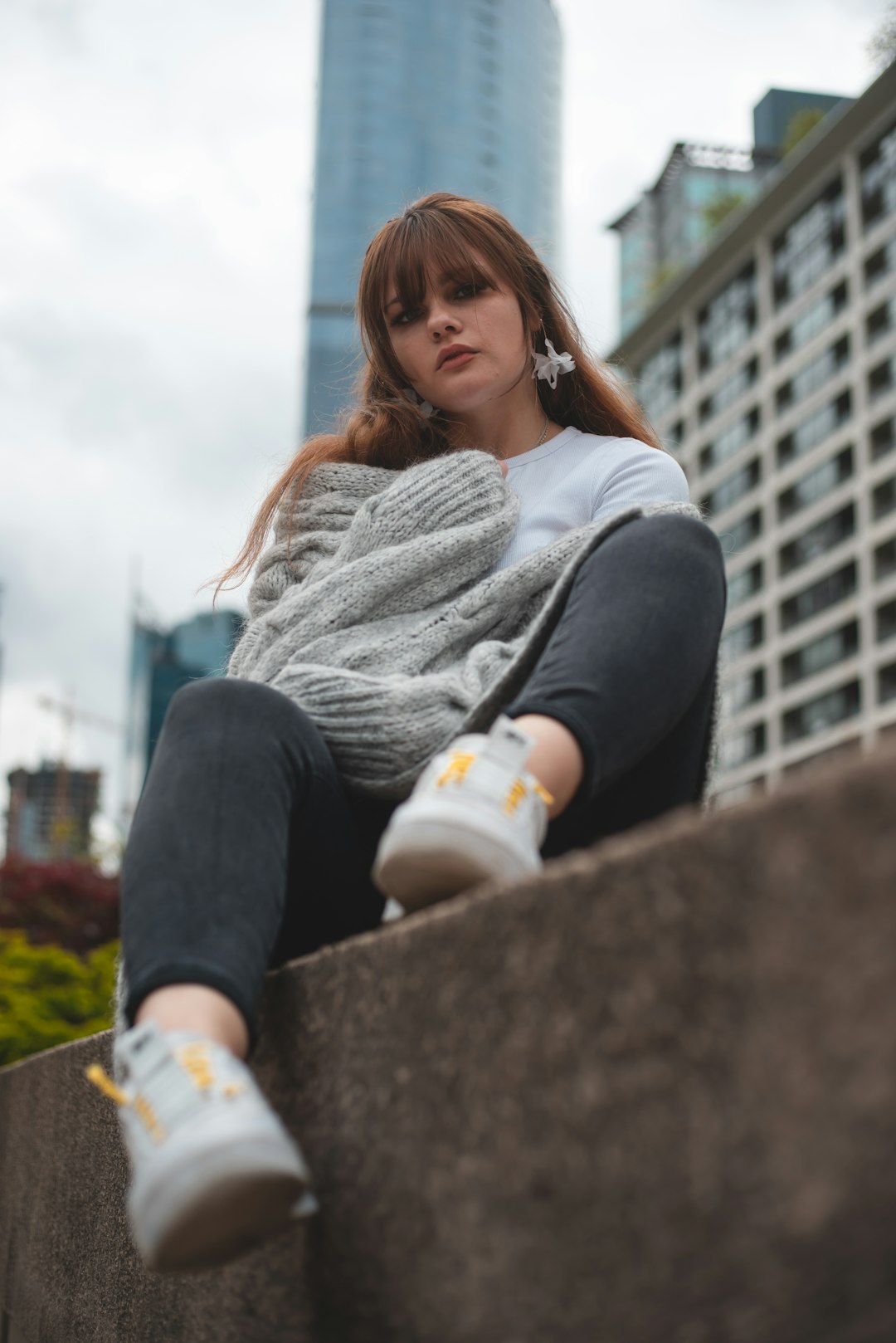 woman in gray sweater and black pants sitting on concrete wall during daytime