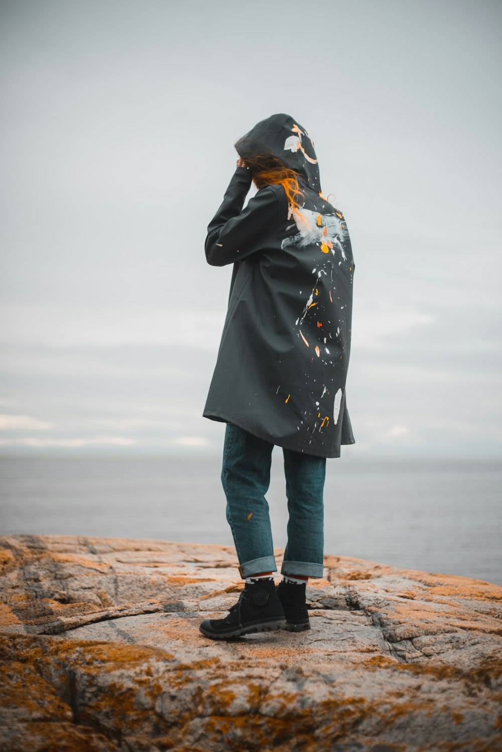 person in black coat and blue denim jeans standing on brown rock formation during daytime