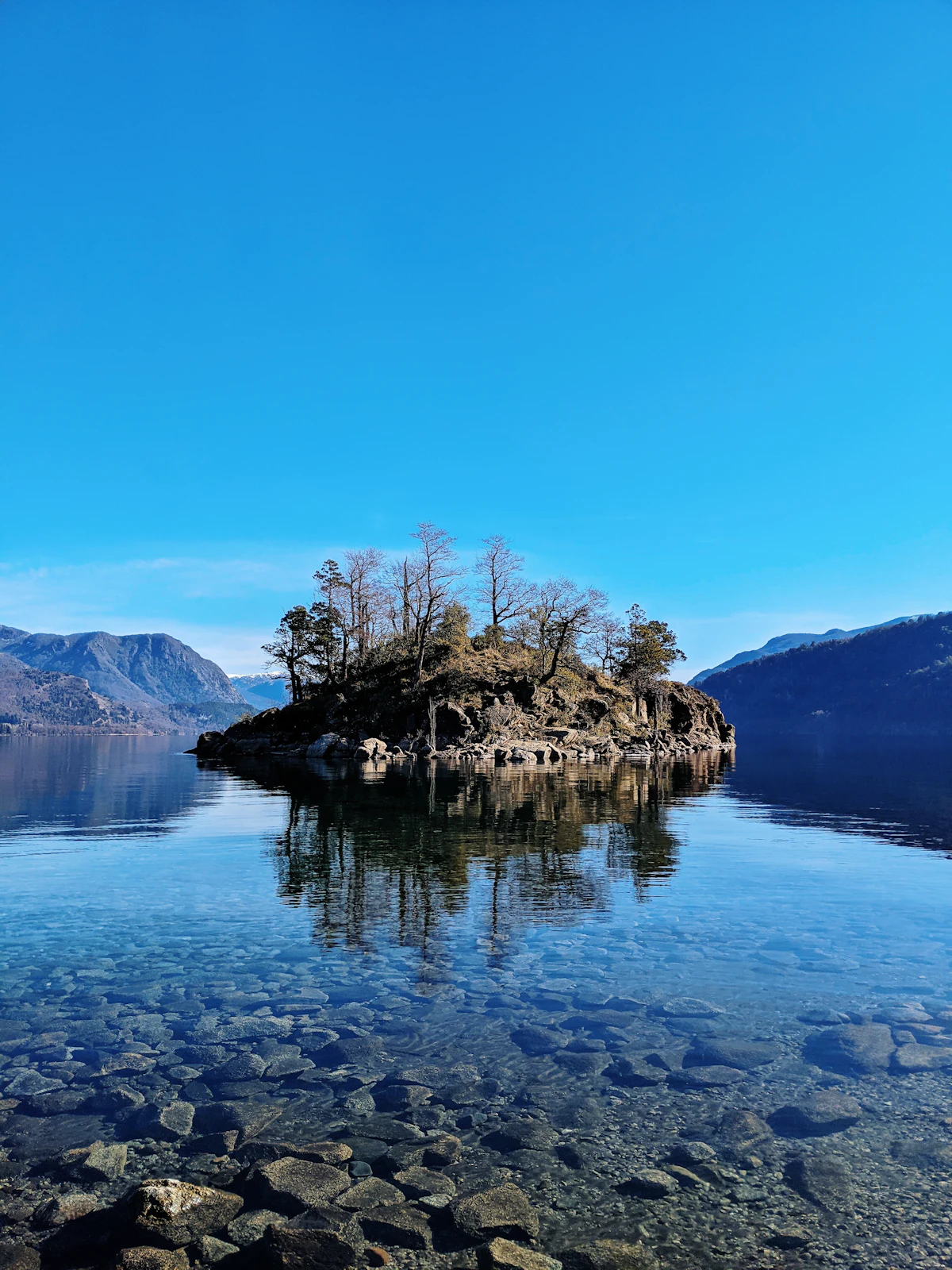 A rocky islet with a few trees in clear lake water near San Martín de los Andes