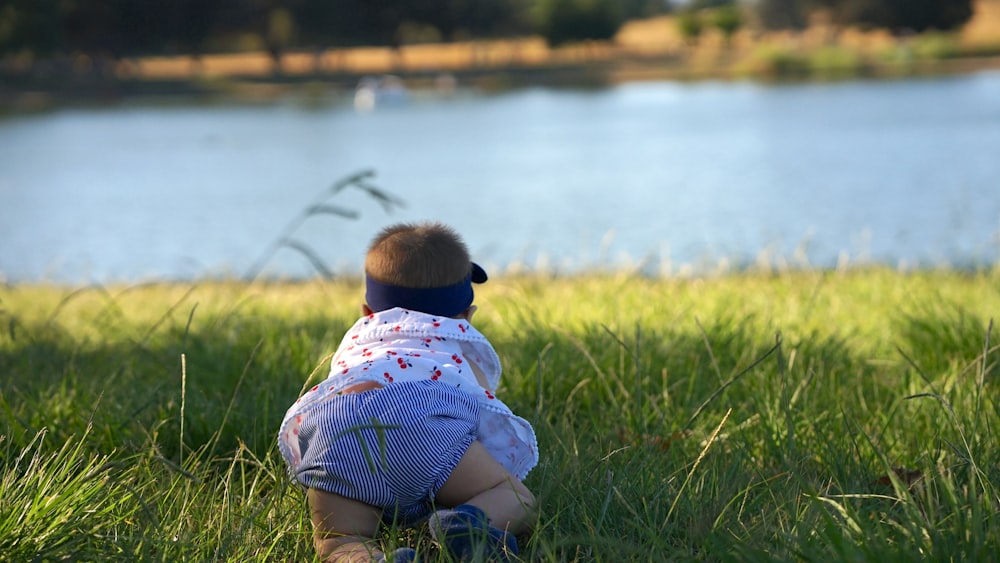 child in green and white stripe shirt sitting on green grass field near body of water